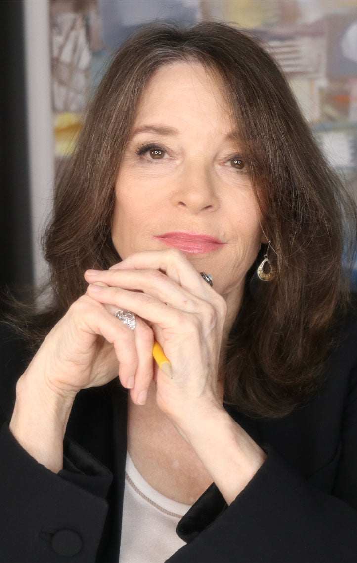 Marianne Williamson sits at her desk with her hands holding a pencil.